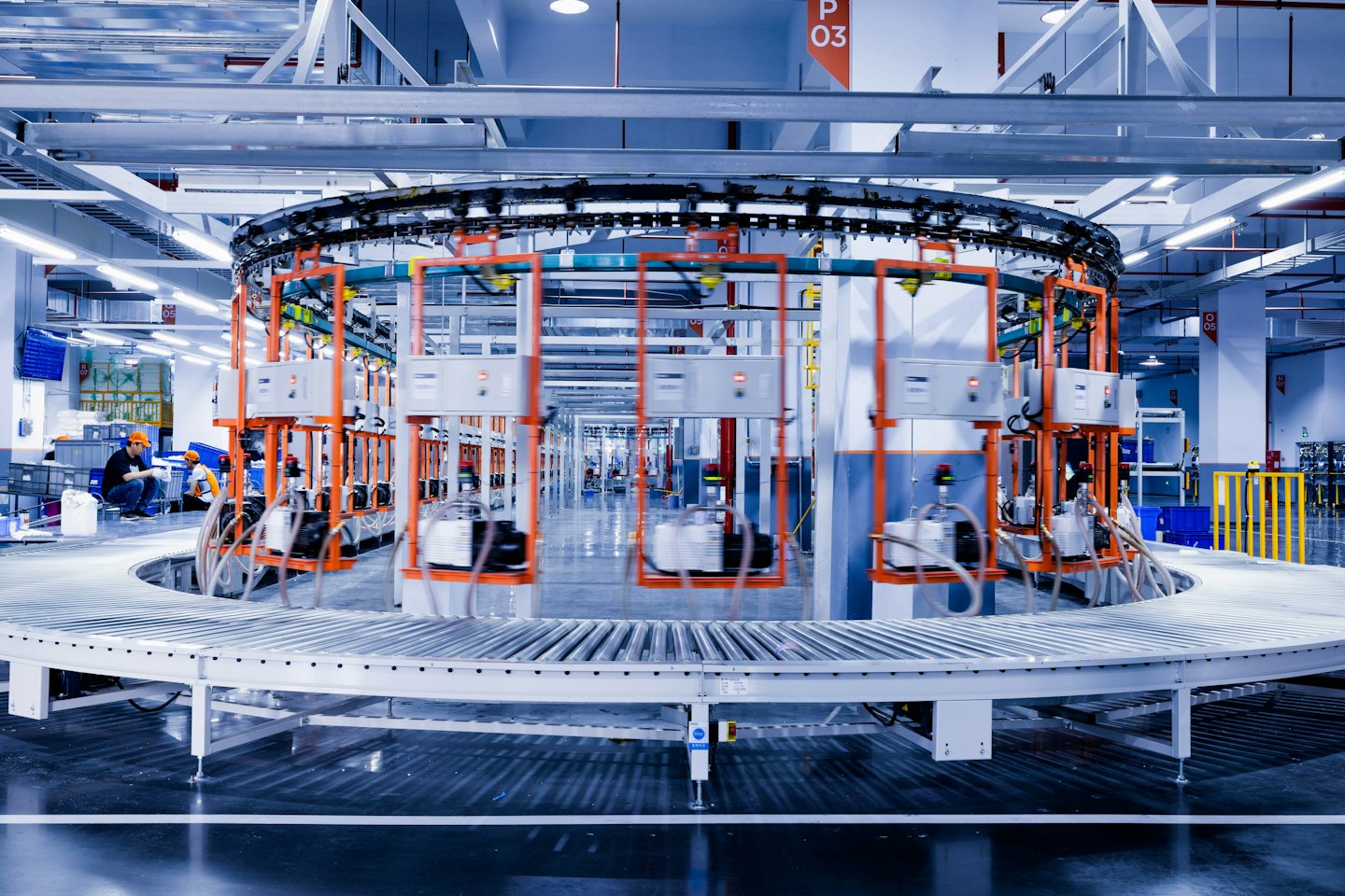 Factory workers oversee a busy automated conveyor system with robotic arms.